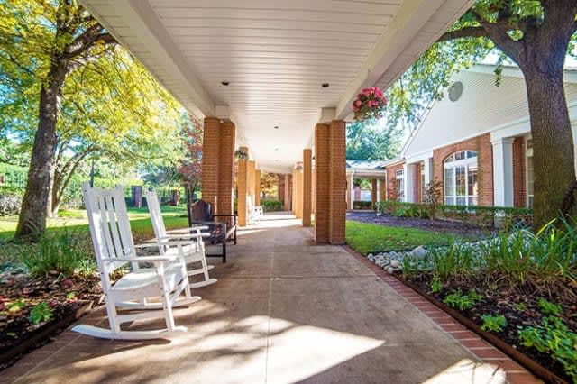 A serene outdoor walkway with rocking chairs and lush garden surroundings.