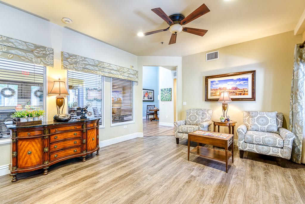 A cozy and well-decorated living room featuring wood flooring, a ceiling fan, stylish furniture, and elegant artwork.
