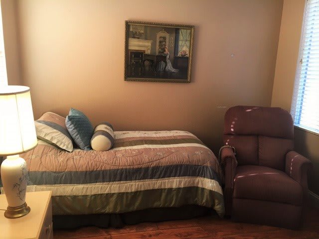 A cozy bedroom with a bed, pillows, recliner chair, and a painting on the wall.