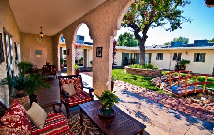 A sunny patio with comfortable seating, arches, and a view of a well-manicured garden courtyard.