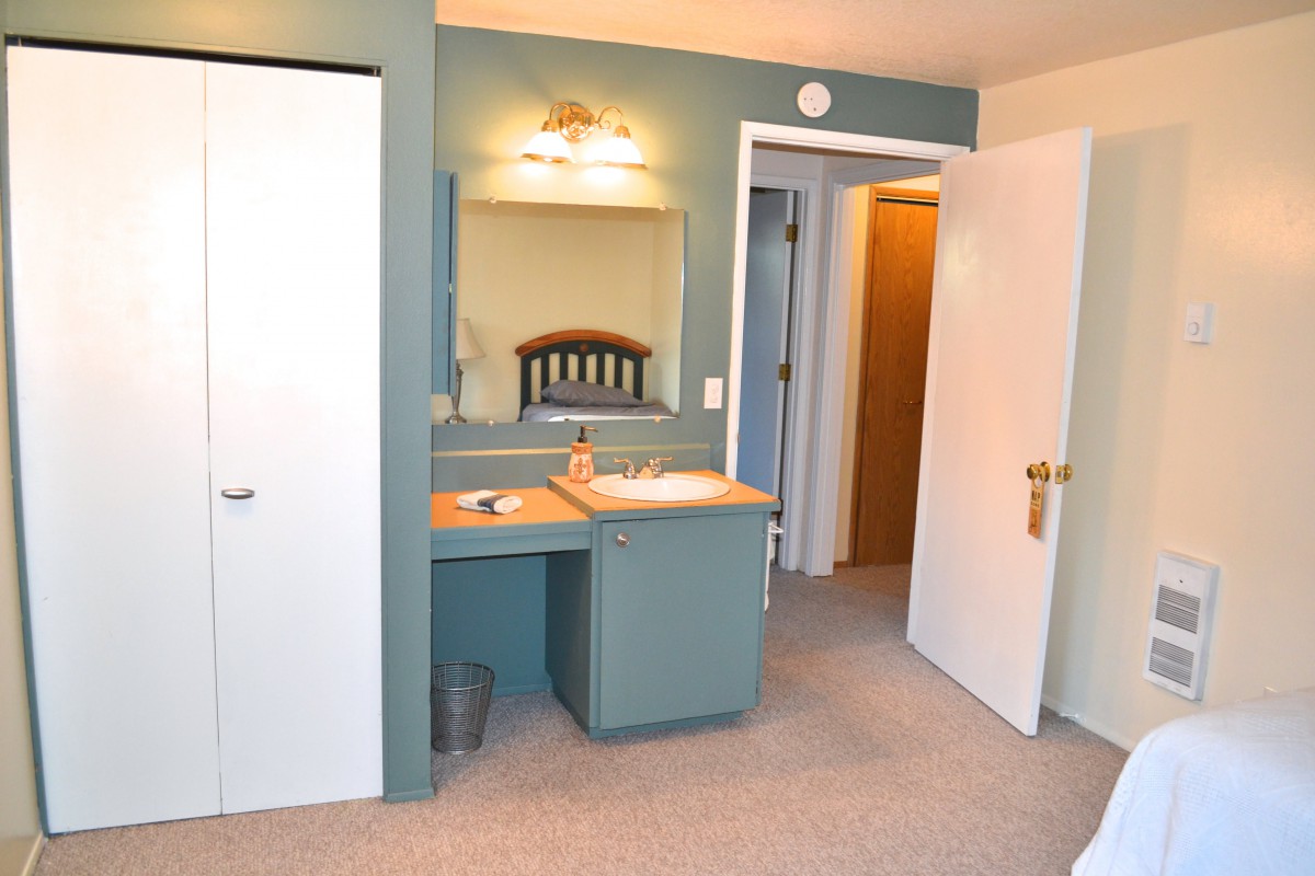 A bathroom interior featuring a vanity with a sink, mirror, carpet flooring, and visible doorways.