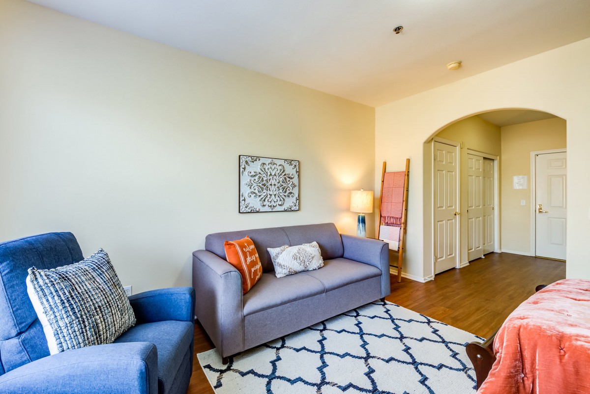 A cozy living room with a gray sofa and a blue armchair, featuring stylish decor and lighting.