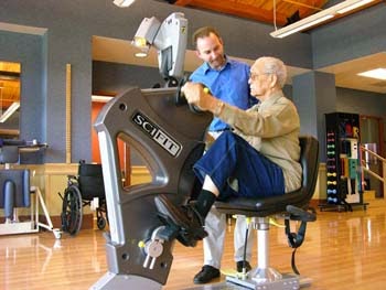 A healthcare professional assists an elderly person using a specialized exercise machine designed for rehabilitation and fitness.