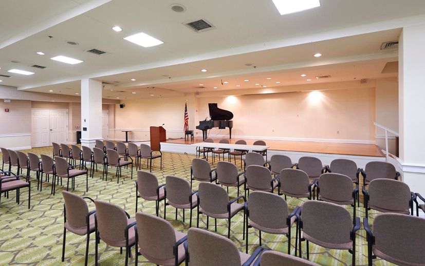 An empty auditorium with a stage featuring a piano and rows of chairs set up for an audience.