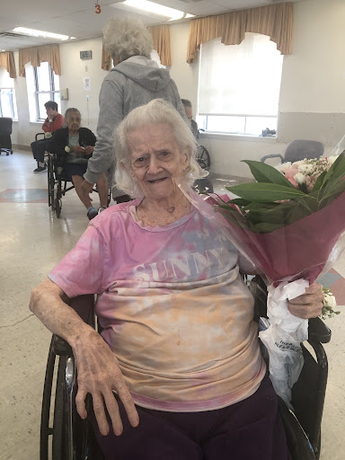 An elderly woman happily holding a bouquet of flowers while seated in a wheelchair.