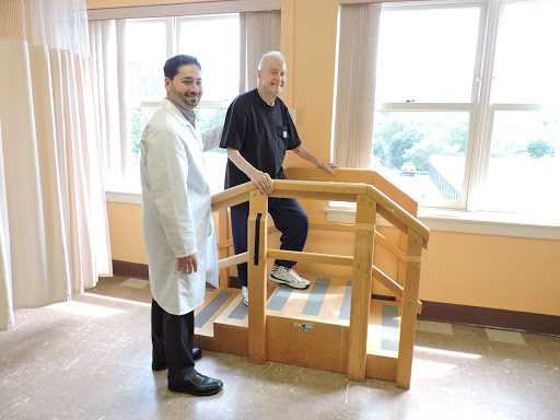 A doctor and a patient are engaged in rehabilitation exercises, using a stair model to assist with physical therapy.