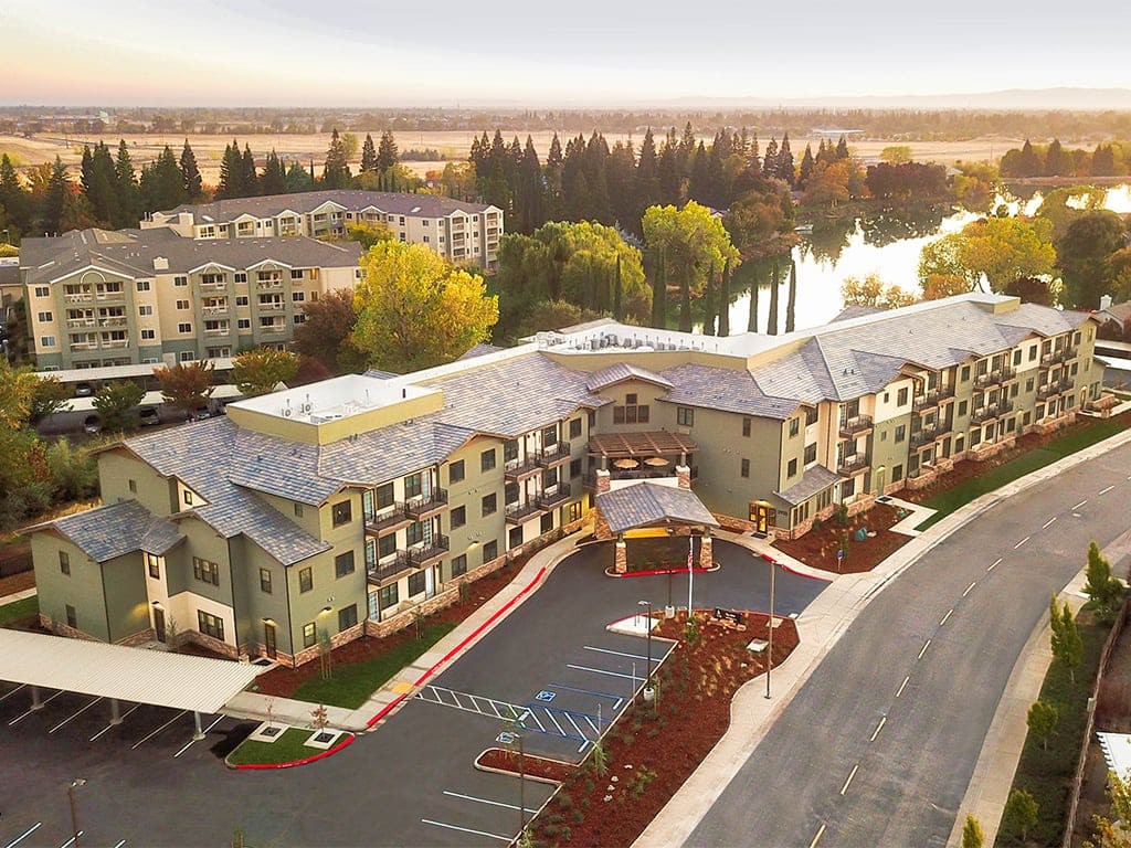 An aerial view of a residential complex surrounded by natural scenery and a nearby water body.