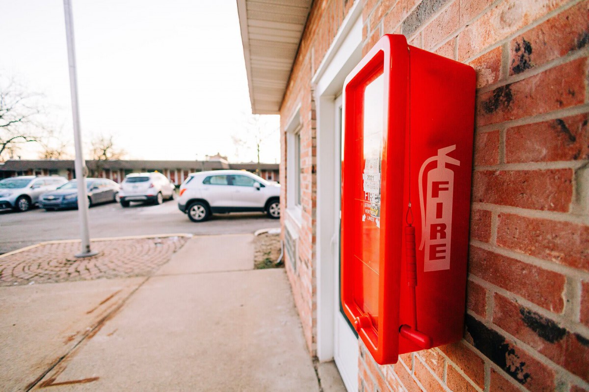 A fire extinguisher box is mounted on the wall outside a building near a parking lot.