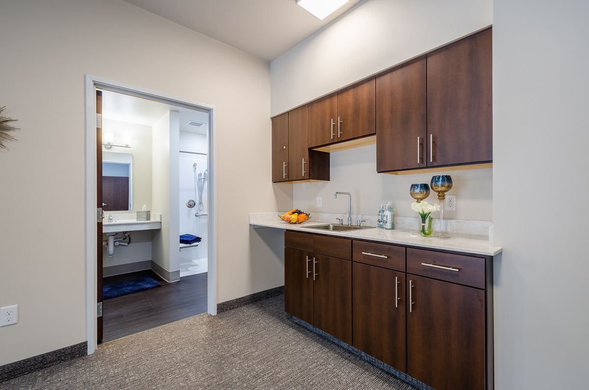 A modern kitchen with sleek cabinets and a clean countertop, leading into a well-lit adjoining room.
