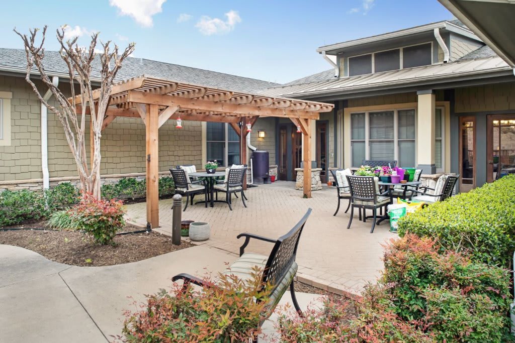 A cozy outdoor patio area featuring a wooden pergola, seating arrangements, and vibrant landscaping.