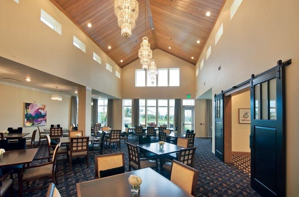 A well-lit dining area with elegant chandeliers and high ceilings, featuring neatly arranged tables and chairs.