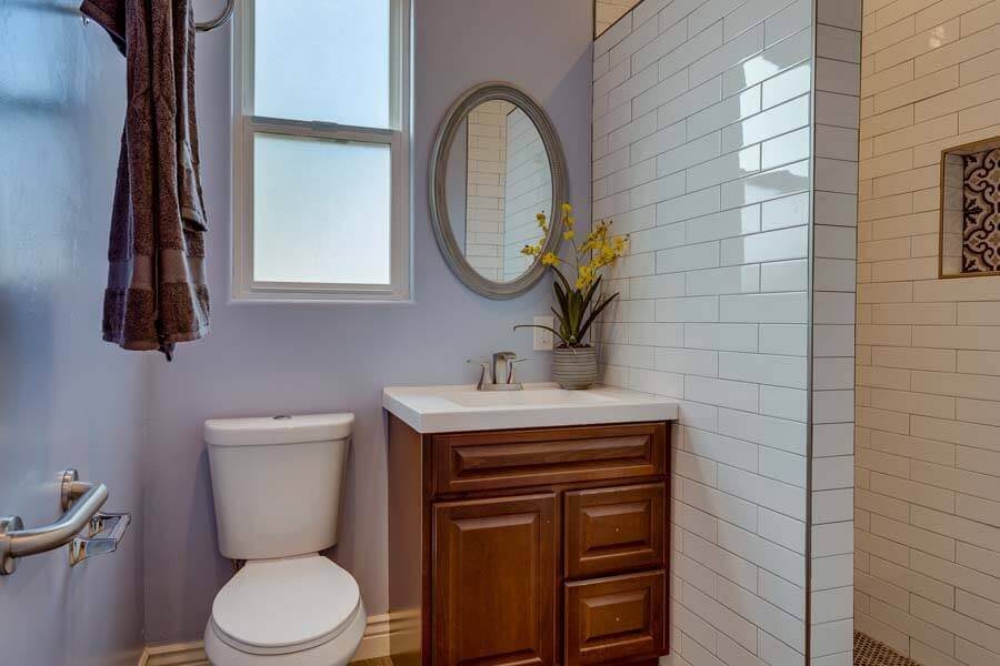 A small bathroom featuring a vanity with a round mirror, a toilet, and white tiled walls.