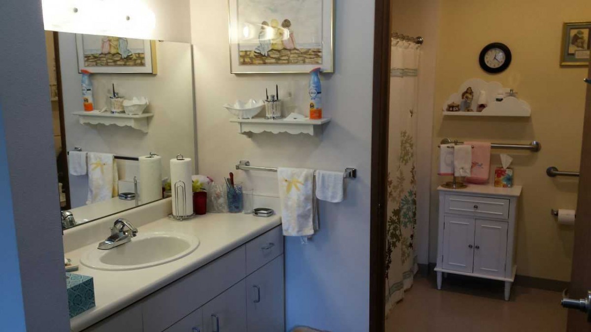 A clean and organized bathroom featuring a sink, mirror, and neatly arranged toiletries on a shelf.