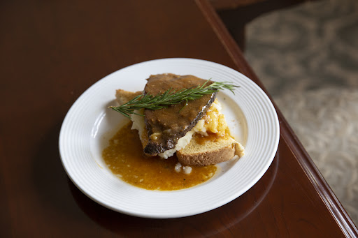 A beautifully plated dish featuring meat on a bed of mashed potatoes, garnished with fresh herbs and accompanied by a savory sauce.