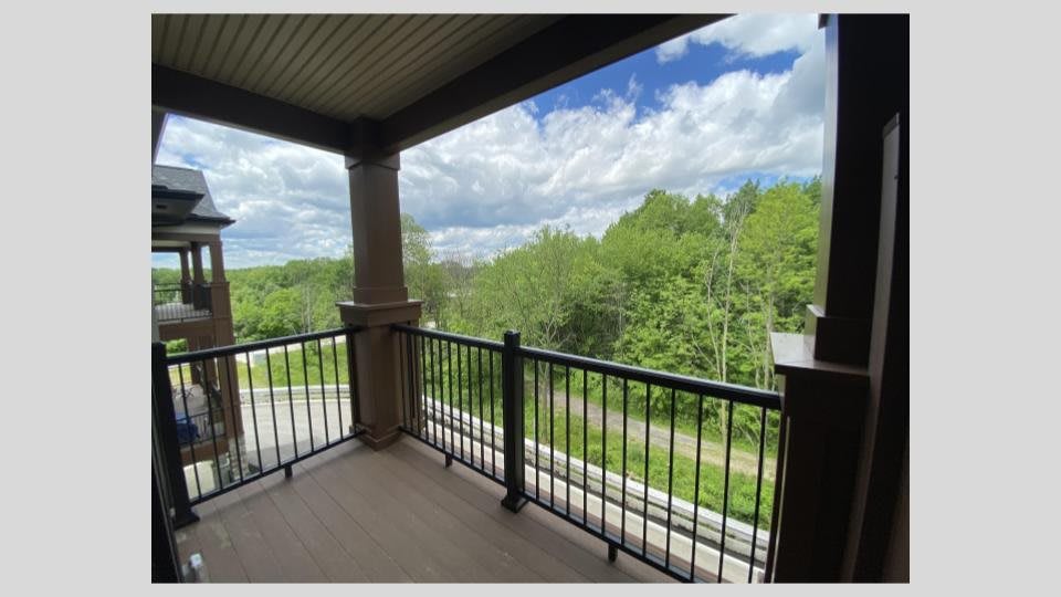 A spacious balcony with a view of lush green trees and a partly cloudy sky.