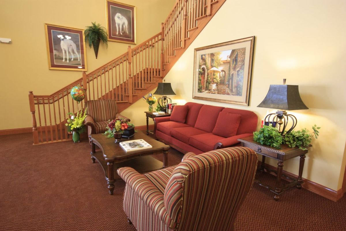 A cozy living room featuring a red sofa, striped armchair, and wooden staircase, adorned with artwork and decorative plants.