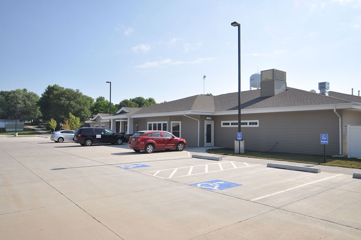 A small commercial building with a parking lot featuring several parked cars on a bright day.