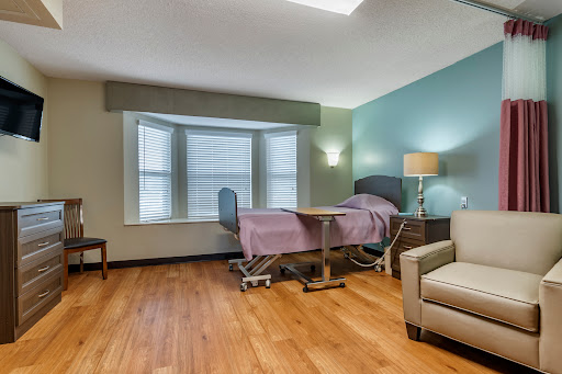 A well-lit hospital patient room featuring a bed, a window with blinds, and comfortable furniture.