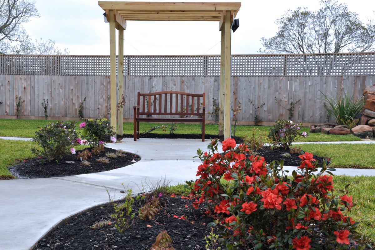 A serene garden setting featuring a wooden bench under a pergola, surrounded by vibrant flowers and a winding pathway.