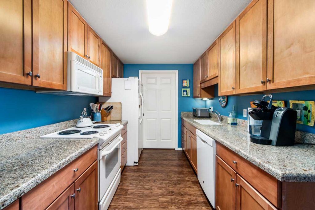 A galley kitchen with wooden cabinets, modern appliances, and blue walls.