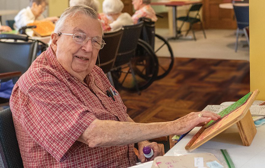 An elderly man engages in painting at a senior center, expressing his creativity.
