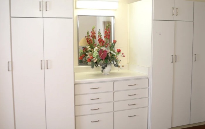 A white cabinet with a mirror and a vase of flowers on the counter.