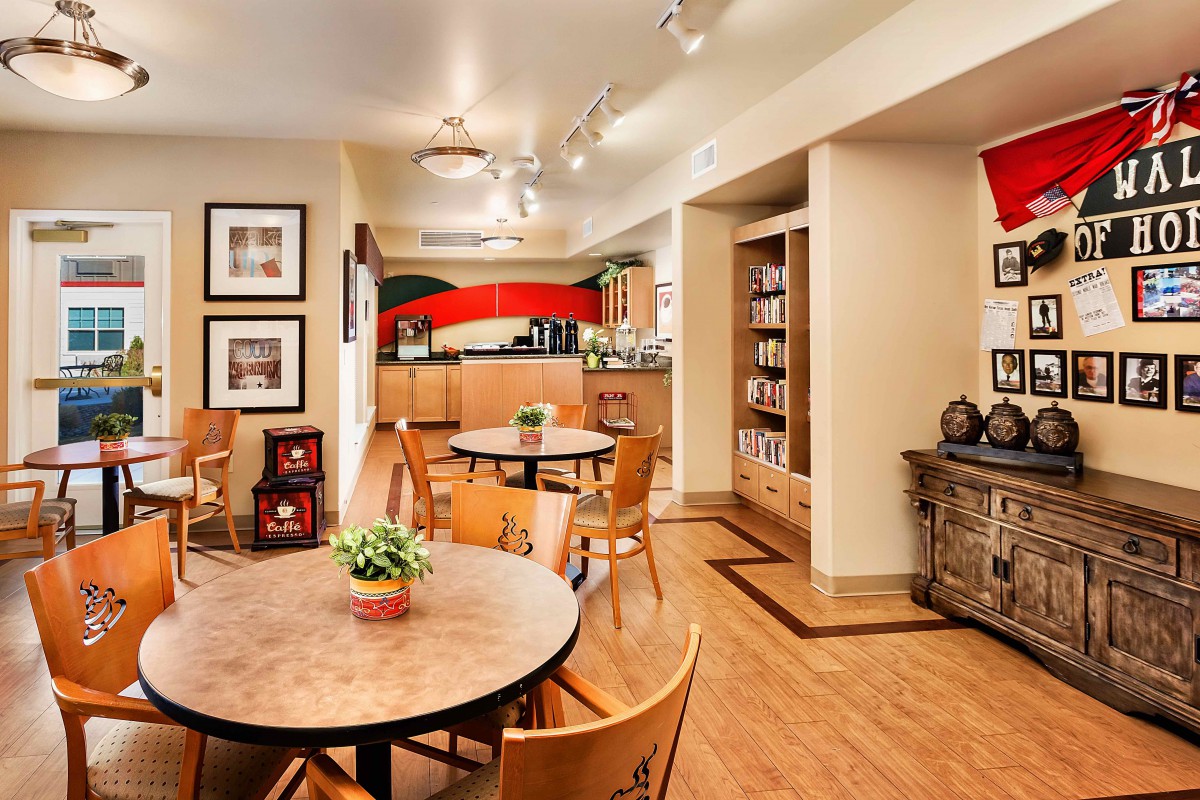 A cozy dining area with round tables and wooden chairs, leading into a kitchen with vibrant artwork and well-organized shelves.
