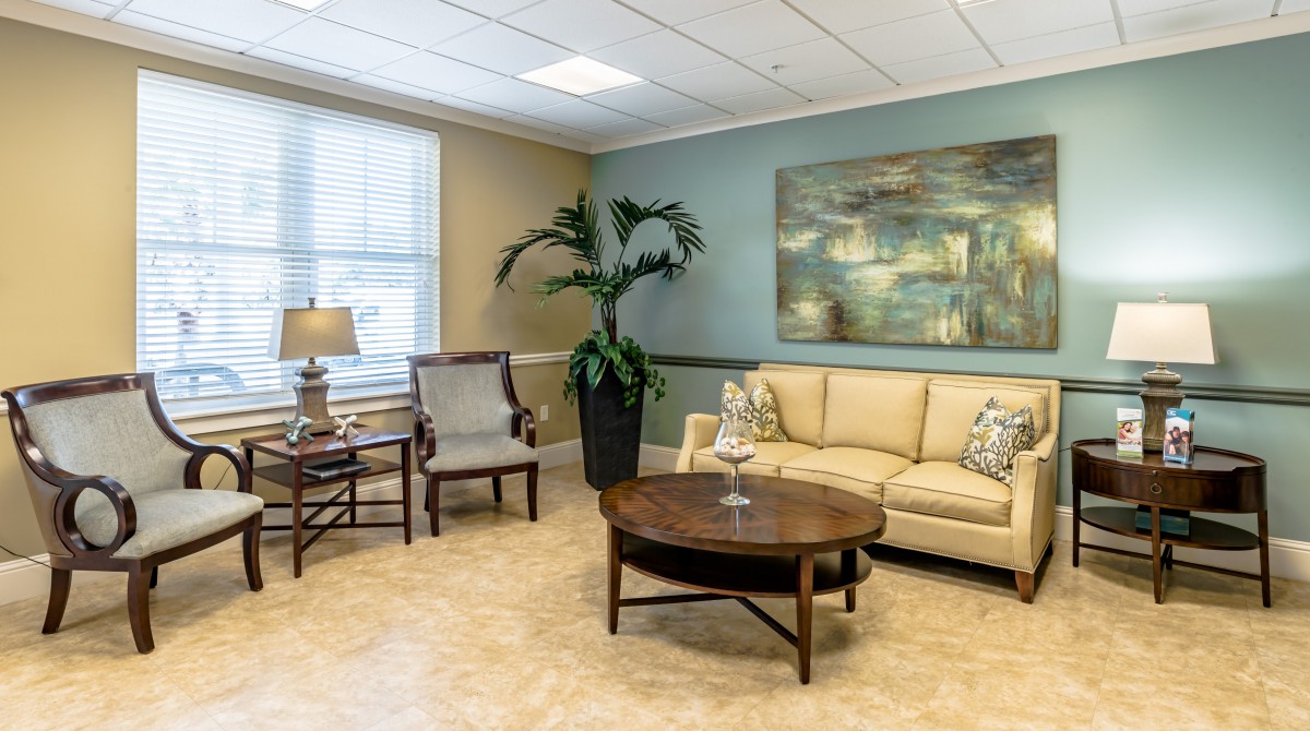 A cozy living room with a sofa, armchair, coffee table, and decorative elements including a painting and a large potted plant.