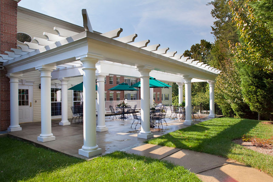 A scenic outdoor patio area with a pergola and green umbrella-shaded tables, surrounded by lush greenery.
