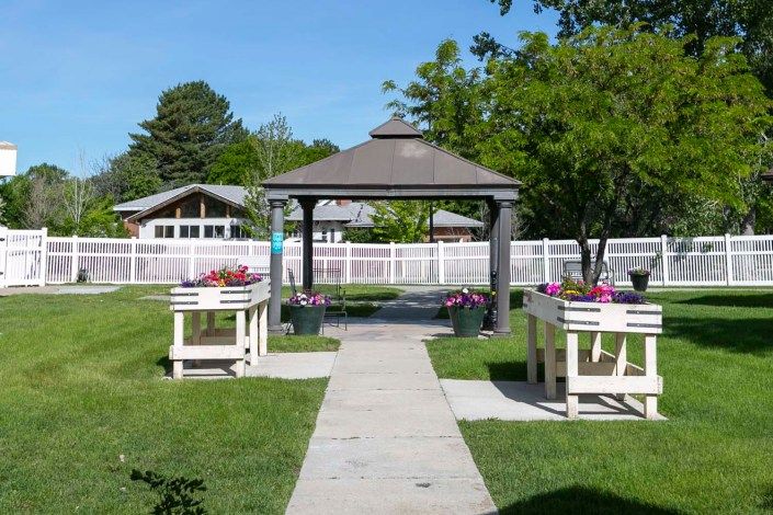 A serene garden with a pathway leading to a wooden gazebo, surrounded by flowers and trees.