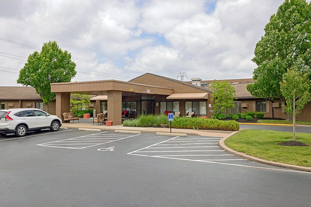 A building with a parking lot in front, surrounded by greenery under a cloudy sky.