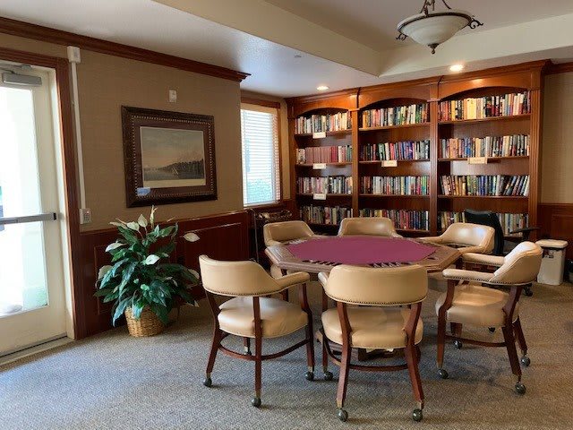 A cozy library space with a table surrounded by chairs and bookshelves filled with books.