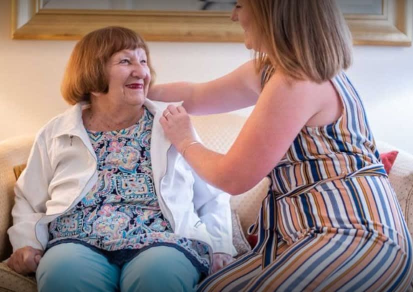 A caregiver assists an elderly woman, sharing a joyful moment indoors.