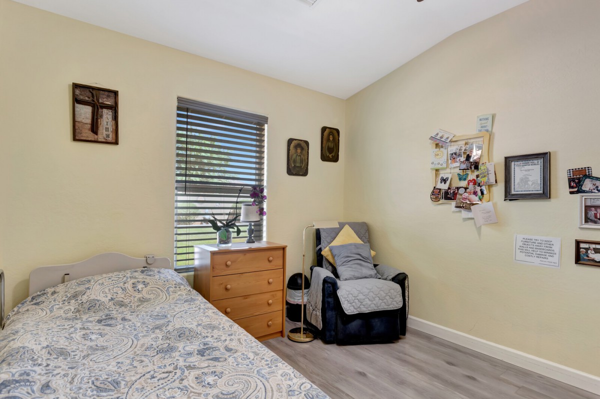 A cozy bedroom with a bed, armchair, dresser, and window.