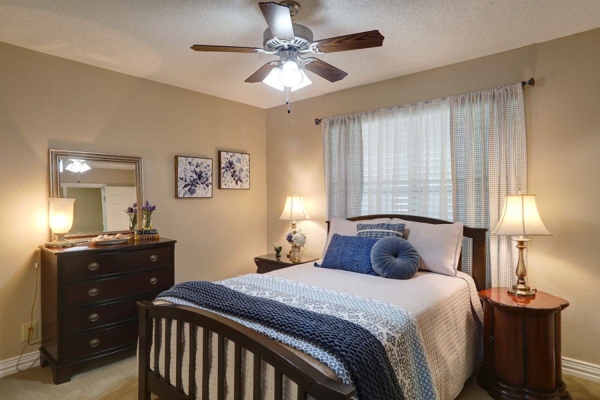 A cozy bedroom featuring a neatly made bed with blue and white linens, a dresser with a mirror, and a ceiling fan overhead.
