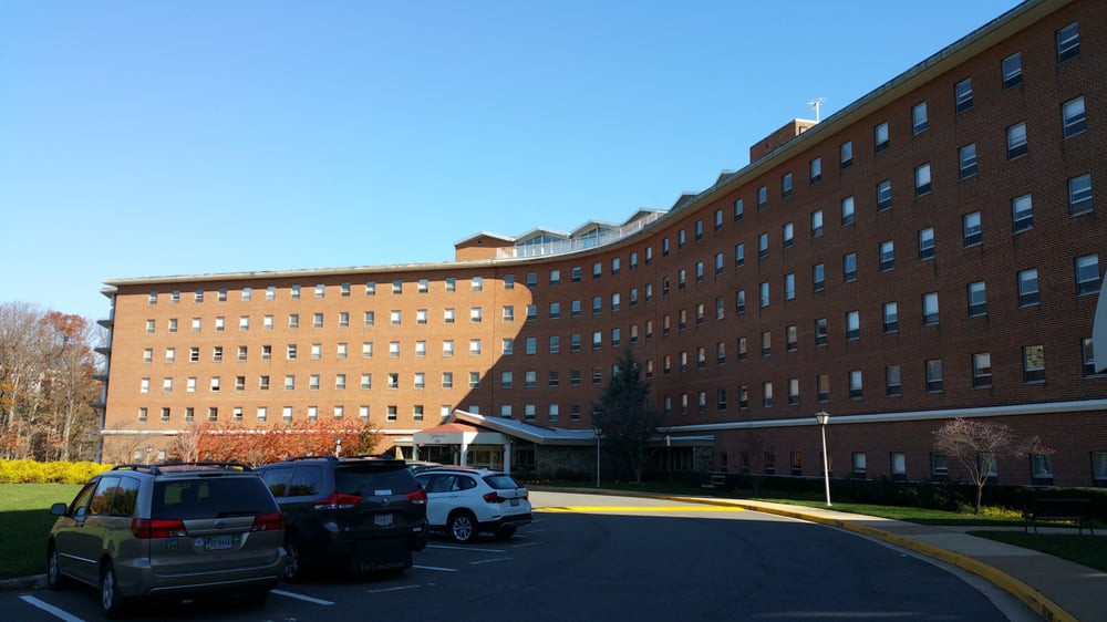 A curved brick building with multiple windows, surrounded by a parking lot on a sunny day.