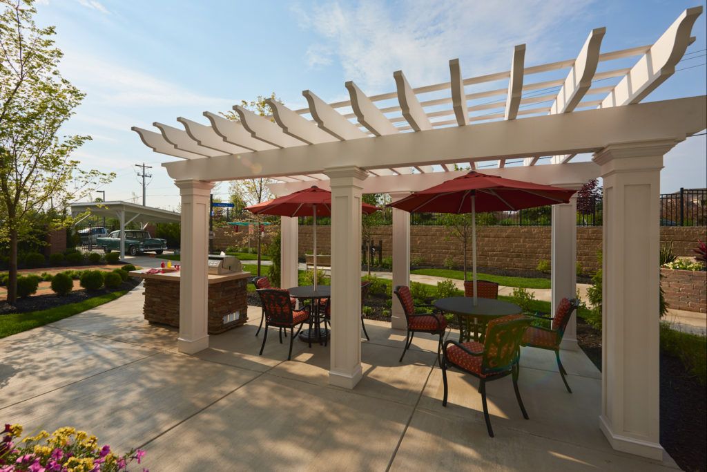 A pleasant outdoor patio area with a pergola, tables, and chairs under umbrellas on a sunny day.