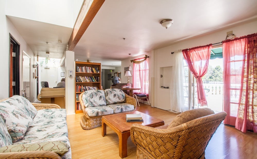 Cozy living room with wooden flooring, featuring a floral sofa set and a bookshelf.