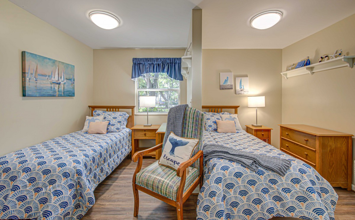 A cozy bedroom with twin beds, featuring blue patterned bedding and a comfortable armchair.