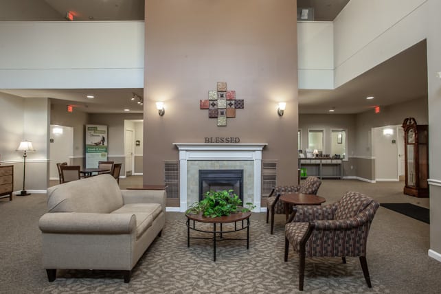 A cozy living room with a fireplace, sofa, and chairs arranged around a central coffee table with indoor plants.