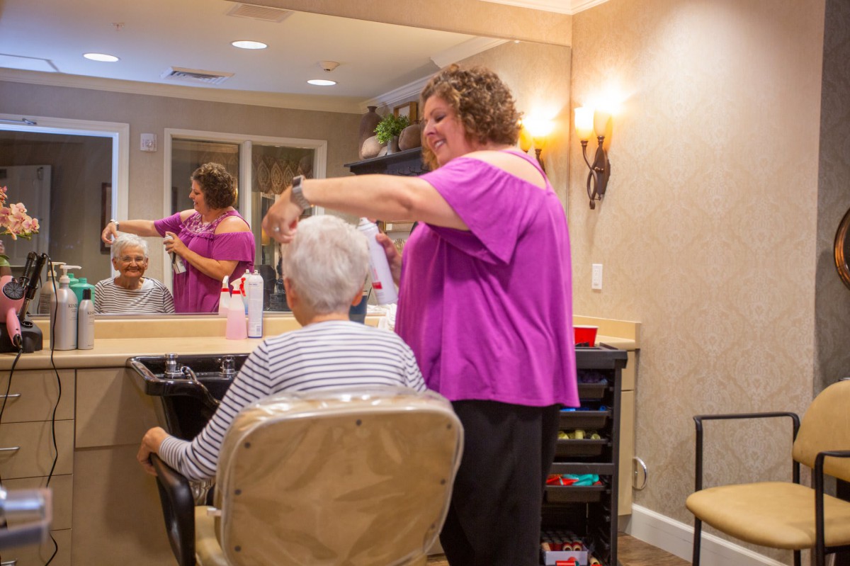 A hair stylist tends to an elderly client's hair in a cozy salon setting.