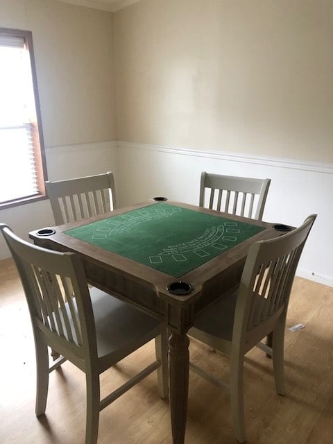 A dining area featuring a square green felt game table with four chairs.
