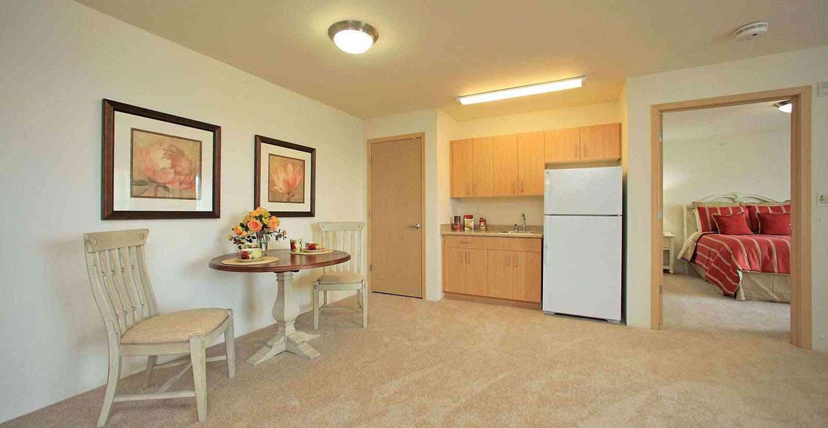 A cozy kitchen and dining area with a table, chairs, fridge, and cabinets.