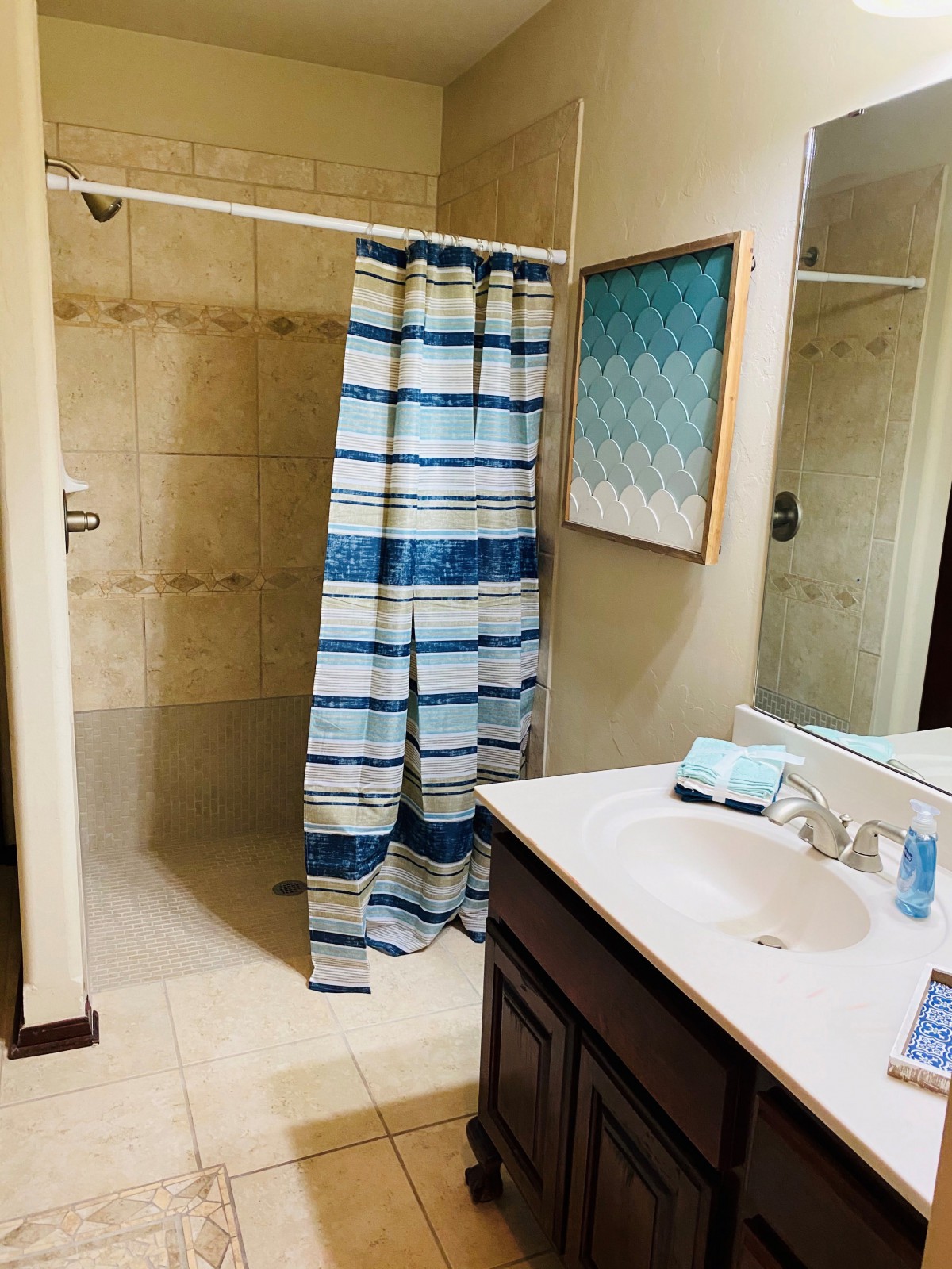 A bathroom featuring a shower with a blue and white striped curtain, a sink with toiletries, and a piece of artwork on the wall.