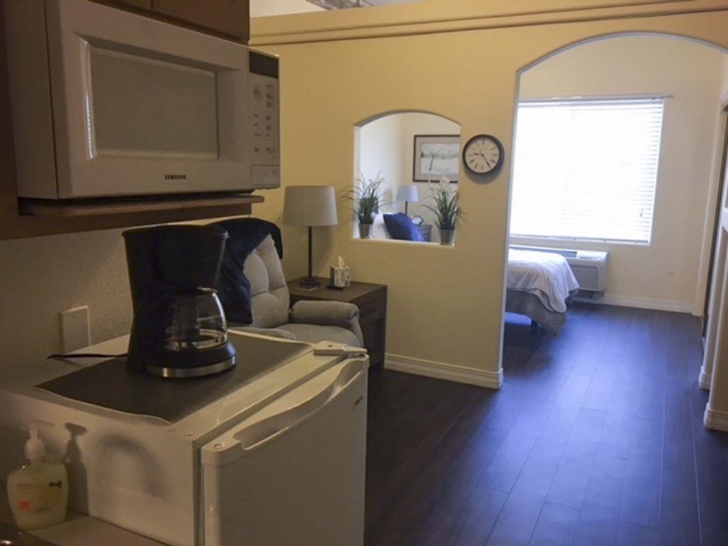 A view of a studio apartment featuring a compact kitchen area with a coffee maker and microwave, leading into a living space and bedroom.