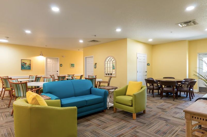 A cozy living room with colorful furniture and a dining area in the background.