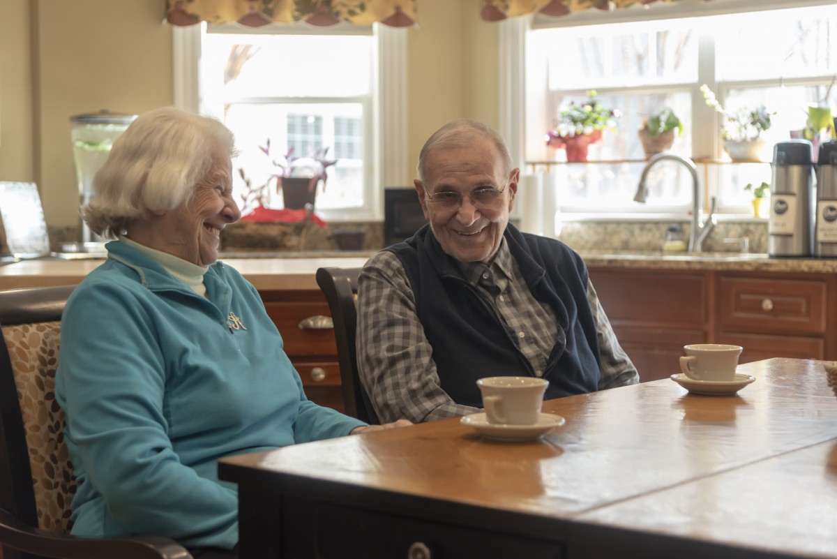 An elderly couple sitting at a kitchen table enjoying a conversation over tea.