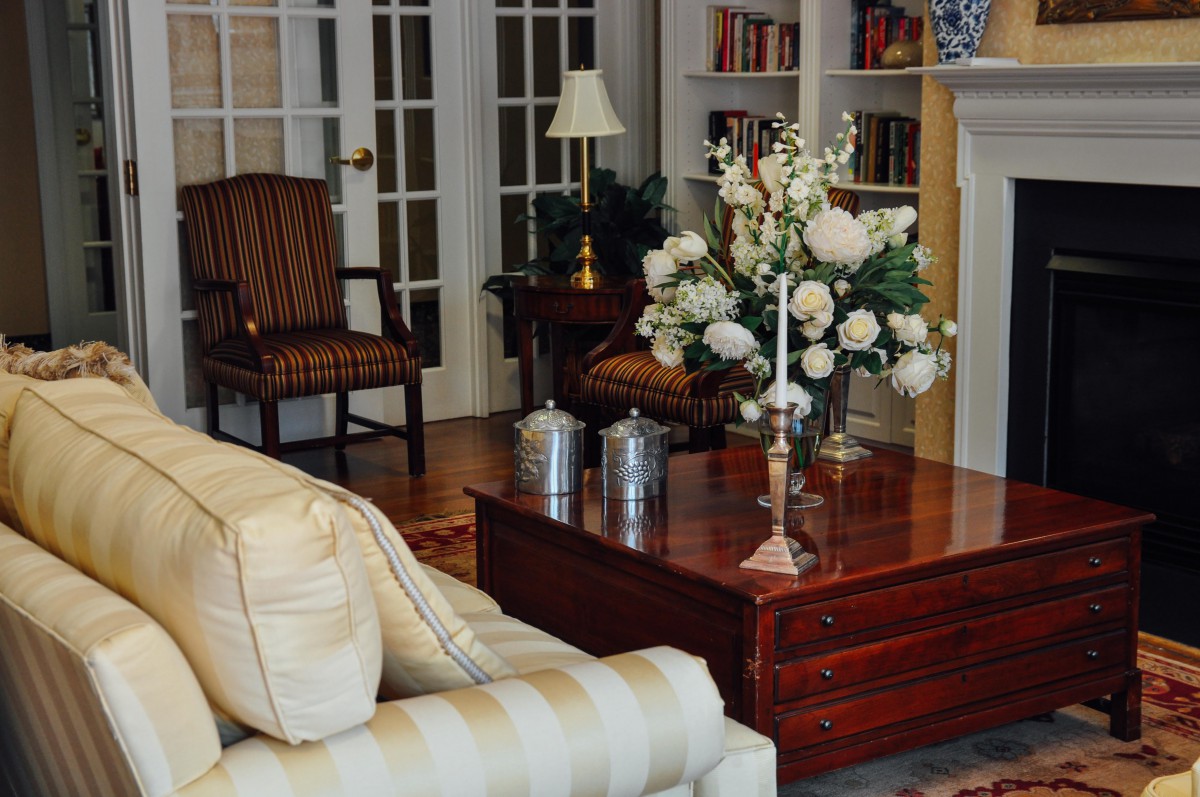 A cozy living room with elegant furnishings, featuring a sofa, coffee table with floral arrangement, and a bookshelf in the background.
