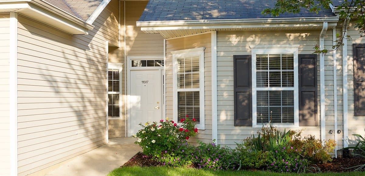 A cozy house exterior with a white front door, surrounded by windows and well-maintained landscaping.