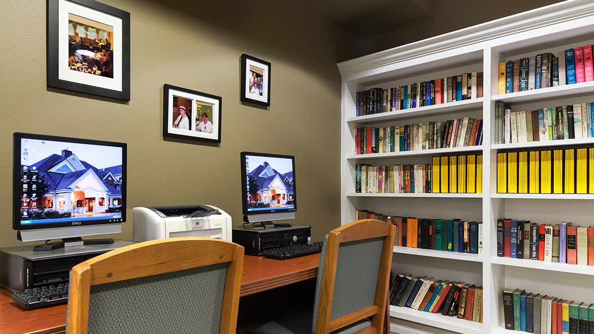 A cozy office space with a computer and printer on the desk, surrounded by a bookshelf filled with books.
